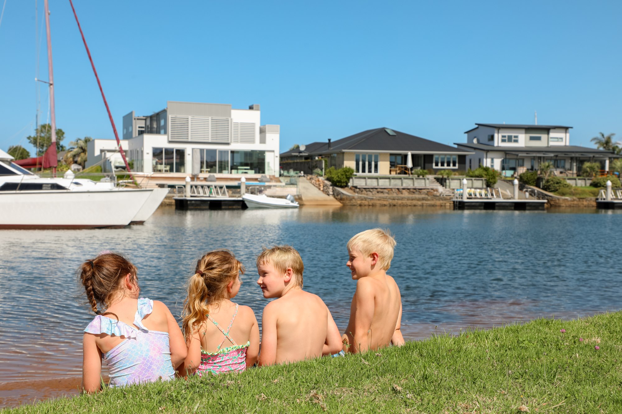 Four happy kids sitting on canal infront of luxury houses and boats